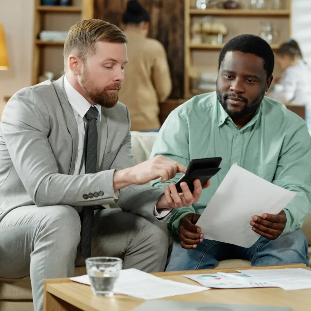 Two men sitting on a couch with one holding a calculator